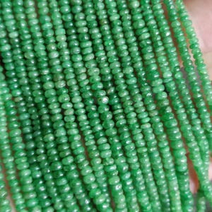 May include: Strands of small, round, bright green beads. The beads are strung together, creating multiple parallel lines. The beads have a slightly irregular shape and a polished appearance. The overall effect is a vibrant, textured display of gemstone beads.