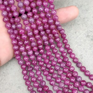May include: A strand of pink faceted gemstone beads. The beads are round and have a smooth, polished finish.