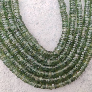 May include: A strand of green gemstone beads, each bead is faceted and has a slightly rounded shape. The beads are strung together to form a long necklace.