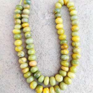 May include: A strand of green and yellow gemstone beads. The beads are round and have a smooth, polished finish.