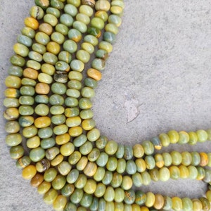 May include: A strand of green and yellow gemstone beads. The beads are round and have a smooth, polished finish. The beads are strung on a clear thread.