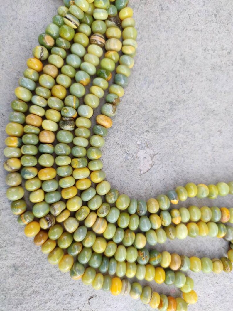 May include: A strand of green and yellow gemstone beads. The beads are round and have a smooth, polished finish. The beads are strung on a clear thread.