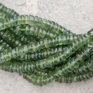 May include: A strand of green gemstone beads, each bead is faceted and has a cylindrical shape.