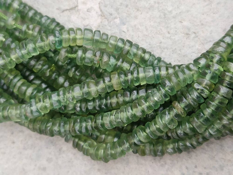 May include: A strand of green gemstone beads, each bead is faceted and has a cylindrical shape.