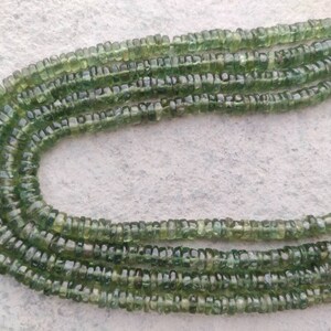 May include: A strand of green gemstone beads, each bead is faceted and has a slightly irregular shape. The beads are strung on a clear thread and are arranged in a loose, flowing pattern.