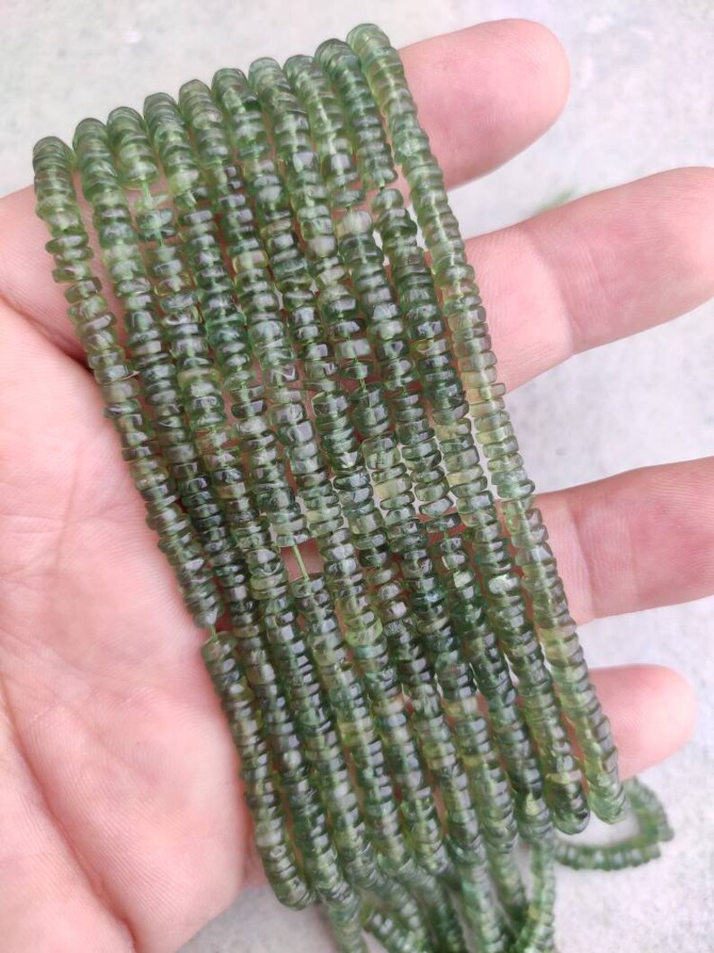 May include: A strand of green gemstone beads, each bead is faceted and has a slightly irregular shape. The beads are strung on a clear thread and are approximately 4mm in diameter.