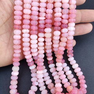 Peut inclure: Un brin de perles de pierres précieuses roses et blanches. Les perles sont rondes et ont une surface texturée.