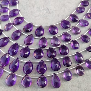 May include: A strand of purple amethyst gemstone beads in a teardrop shape. The beads are strung on silver wire.