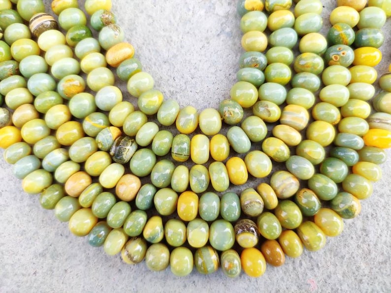 May include: A strand of green and yellow gemstone beads. The beads are smooth and round, and they have a natural, organic look.
