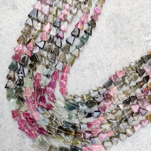 以下が含まれることがあります： 多色でファセットカットされた三角形の宝石ビーズのストランド。ビーズはピンク、グリーン、ブラックのミックスです。