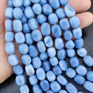 Puede incluir: Una hebra de cuentas de piedras preciosas ovaladas de color azul claro. Las cuentas son lisas y pulidas, con un ligero brillo iridiscente.