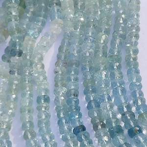 Puede incluir: Hebras de cuentas de piedras preciosas de aguamarina en varios tonos de azul y transparente. Las cuentas facetadas reflejan la luz y están ensartadas. La imagen muestra múltiples hebras, creando un efecto texturizado. El tema general son las joyas y las piedras preciosas.