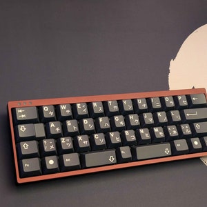 Puede incluir: Un teclado mecánico compacto, rojo y negro, con teclas japonesas. El teclado tiene una fila de teclas de función, una fila de teclas numéricas y una fila de teclas de letras. El teclado también tiene una fila de teclas de flecha y una fila de teclas de control.