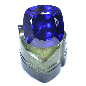 May include: A large, deep blue gemstone with a cushion cut, displayed on a green stone stand.