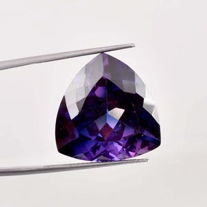 Puede incluir: Una piedra preciosa púrpura facetada con forma triangular.