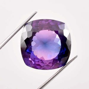 Puede incluir: Una gran gema de talla cojín con un degradado de tonos morados y azules. La gema está facetada y tiene un alto pulido.