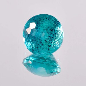 May include: A round, faceted gemstone with a teal blue color. The gemstone is reflecting light, creating a sparkling effect.