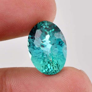 May include: A vibrant teal oval-shaped gemstone with a faceted cut. The gemstone has a light blue hue and a green tint.