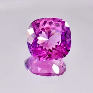 Puede incluir: Una gema púrpura vibrante con un corte cojín, que refleja la luz con un brillo brillante.