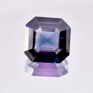 Puede incluir: Una piedra preciosa azul oscuro y púrpura con un corte cuadrado esmeralda.