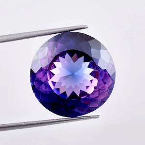 Puede incluir: Una gema redonda y facetada con un degradado de púrpura a azul. La gema tiene un patrón en forma de estrella en el centro.