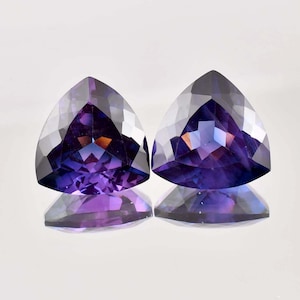 Peut inclure: Deux pierres précieuses taillées en forme de triangle avec un dégradé de couleur violet et bleu. Les pierres précieuses sont facettées et ont un fort éclat.