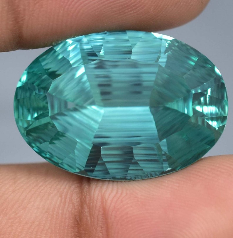 May include: A large, oval-shaped, faceted gemstone with a light blue-green color. The gemstone has a high degree of clarity and brilliance.