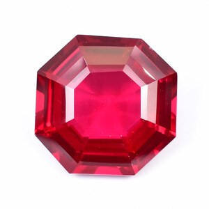 Op de afbeelding: Een gefacetteerde, achthoekig geslepen robijn edelsteen. De edelsteen heeft een levendige, dieprode kleur met meerdere facetten die licht reflecteren. De edelsteen is geplaatst tegen een witte achtergrond.