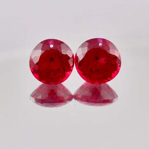 May include: Two round, red gemstones with a faceted cut. The gemstones are set in a bezel setting and have a hole drilled through the top.