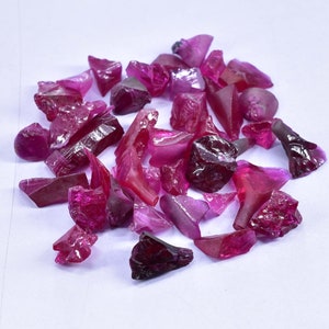 May include: A collection of loose ruby gemstones in various shapes and sizes. The rubies are a deep pink color and have a natural, unpolished finish.