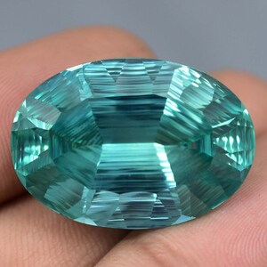 May include: A large, oval-shaped, faceted gemstone with a light blue-green color. The gemstone has a smooth, polished surface and is cut to create a brilliant shine.