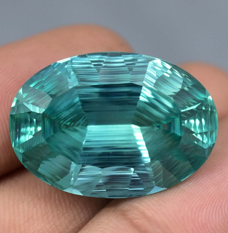 May include: A large, oval-shaped, faceted gemstone with a light blue-green color. The gemstone has a smooth, polished surface and is cut to create a brilliant shine.
