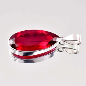 Op de afbeelding: Een traanvormige hanger met een dieprode edelsteen gezet in een zilveren frame.