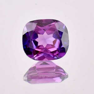 Puede incluir: Una piedra preciosa de talla cojín con un tono púrpura y rosa. La piedra preciosa está facetada y tiene un patrón en forma de estrella en el centro.