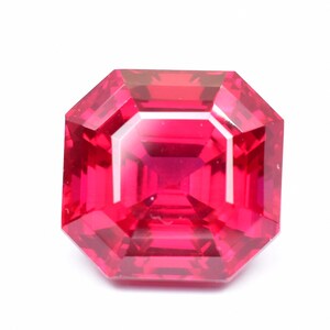 May include: A vibrant red gemstone with a square, octagonal cut. The gemstone is faceted and has a high polish.
