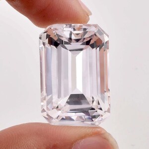 May include: A large, clear, rectangular, faceted gemstone with a pale pink hue. The gemstone is cut in an emerald shape.