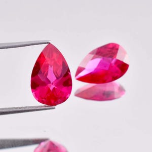 May include: Two pear-shaped, bright pink gemstones. The gemstones are faceted and have a high shine.
