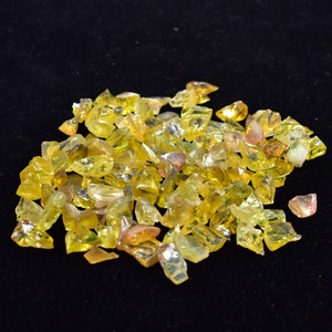 May include: A pile of yellow and green gemstone chips. The chips are irregularly shaped and have a translucent appearance.