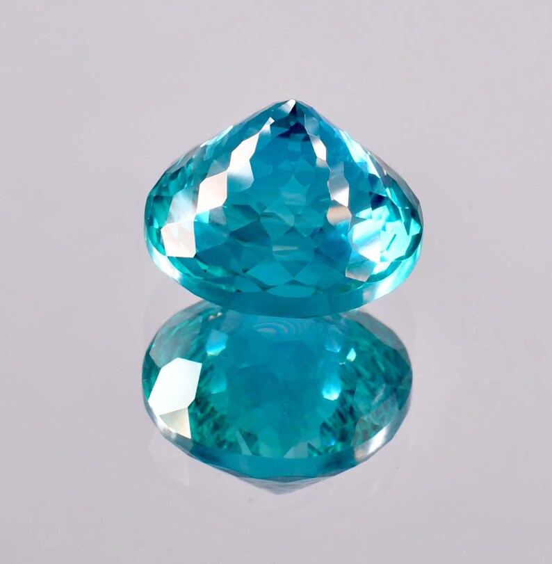 May include: A vibrant blue gemstone with a faceted cut, reflecting light in a dazzling display. The gemstone is oval-shaped and has a pointed top.