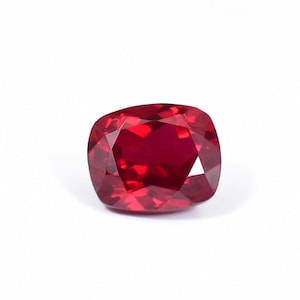 May include: A deep red gemstone with a cushion cut. The gemstone is faceted and has a high polish.