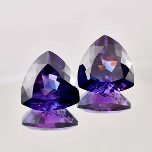 Peut inclure: Deux pierres précieuses facettées triangulaires avec un dégradé de violet à bleu. Les pierres précieuses sont taillées en forme triangulaire et ont un haut poli.