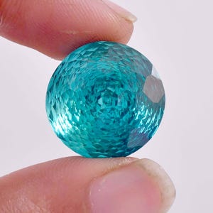 May include: A round, faceted teal blue gemstone with a textured surface.