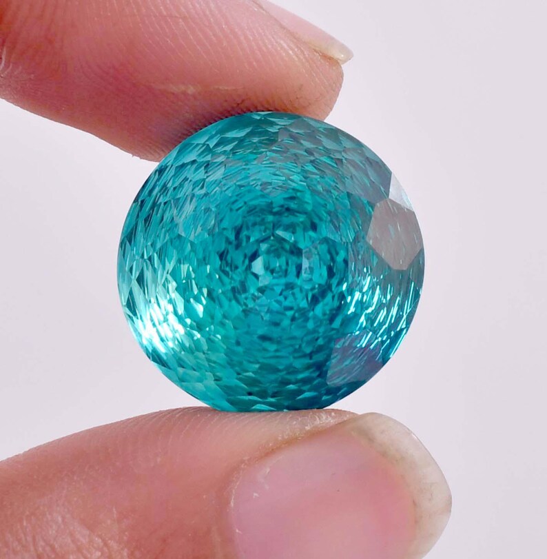 May include: A round, faceted teal blue gemstone with a textured surface.