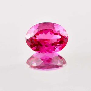 Könnte beinhalten: Ein leuchtend rosa ovaler Edelstein mit facettiertem Schliff. Der Edelstein reflektiert Licht und hat eine glänzende Oberfläche.