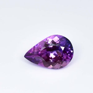 May include: A pear-shaped gemstone with a purple to pink gradient. The gemstone is faceted and has a high polish.