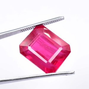 Op de afbeelding: Een levendige roze edelsteen met een rechthoekige smaragd-slijpvorm. De edelsteen wordt vastgehouden door een pincet.