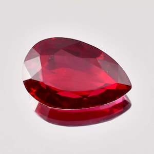 Könnte beinhalten: Ein tief roter birnenförmiger Edelstein mit facettiertem Schliff.