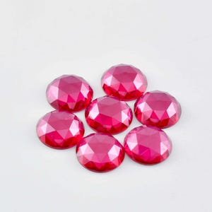 May include: Seven faceted, round, ruby red gemstones. The gemstones are arranged in a loose circle on a white background.