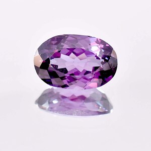 Könnte beinhalten: Ein ovaler Amethyst-Edelstein in tiefem Lila mit facettiertem Schliff. Der Edelstein reflektiert Licht und hat eine glänzende Oberfläche.