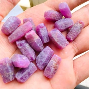 Puede incluir: Una colección de pequeños cristales de piedras preciosas rosadas y moradas sin pulir. Los cristales son de varias formas y tamaños, y tienen un aspecto natural sin pulir.